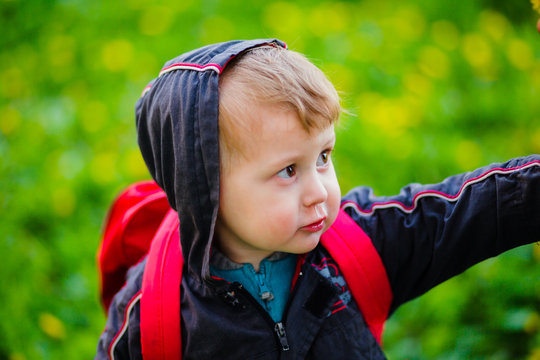Snotty boy on a walk in the spring. Seasonal rhinitis. Allergic reaction to the flowering of dandelions. Child with a backpack.