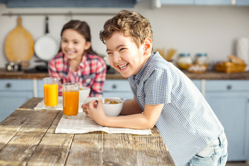 So joyful. Handsome delighted little dark-haired boy laughing and having healthy breakfast with his...