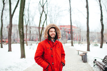 Portrait, close-up of a young stylishly dressed man smiling with a beard dressed in a red winter jacket with a hood and fur on his head. Winter and frost theme © Elizaveta