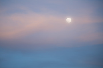 Moon and high wispy clouds tinted pink with evening light