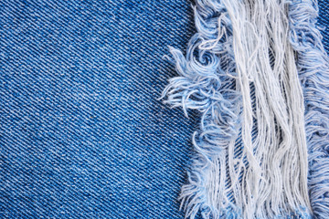 Fragment of jeans trousers with torn, ripped patch, decorated with a hole with threads. Denim background.