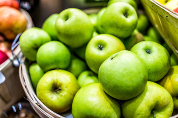 Closeup of many granny smith green yellow apples in wooden basket at farmer's market shop store showing detail and texture - obrazy, fototapety, plakaty