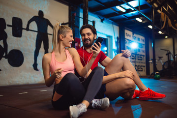 Obraz premium Fit couple in modern crossfit gym with smartphone listening to the music.