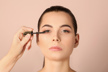 Professional visage artist applying makeup on woman's face against light background