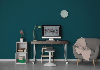Comfortable home workplace with computer on desk against color wall
