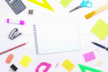 A blank notebook page surrounded by stationery on a white wooden table. Copy the space.