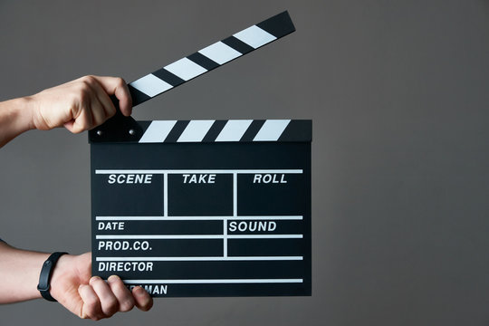 A movie production clapper board. Hands with a movie clapperboard on grey background with copy space, close-up. 