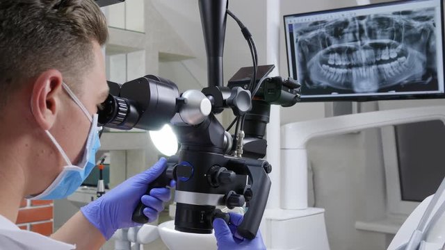 male doctor looks at teeth through dental microscope close-up in clinic, modern technologies in medicine