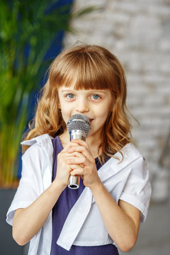 A little beautiful kid sings a song in a microphone. The concept is childhood, lifestyle, music, singing, listening, hobbies.
