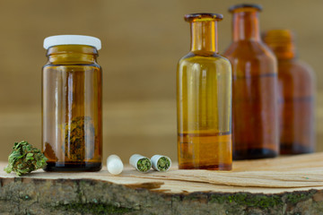 Cannabis medicine - cannabis flower in the  apothecary jar and capsules with marijuana on the fresh natural piece of wood, wooden natural background.