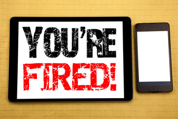 Hand writing text caption inspiration showing You Are Fired. Business concept for Unemployed or Discharge Written on tablet laptop, wooden background with sticky note, coffee and pen