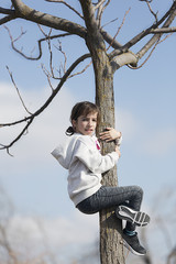 Ten-year-old girl climbing on a tree looking at the camera.