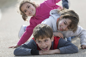 Three children lying on the floor one on top of the other.