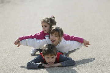 Three children lying on the floor one on top of the other.