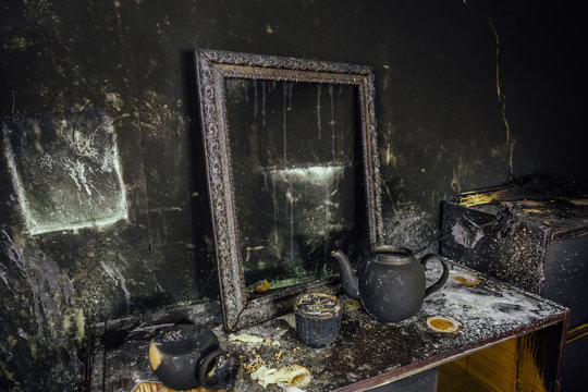 Burnt room interior. Burnt still life. Charred wall, picture frame, pot with burned rose in black soot