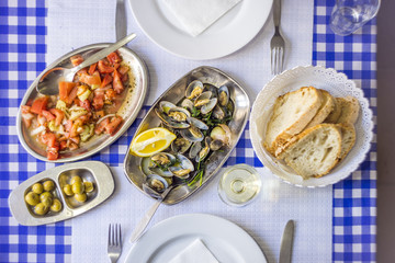 Clams served on silverware, tomato salad, bread, olives and white wine