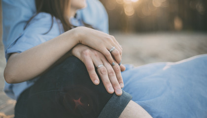 woman and man are sitting on the sand with hands together