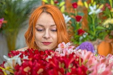 Naklejka na ściany i meble Beautiful redhead Caucasian girl smelling colorful flowers in the garden 
