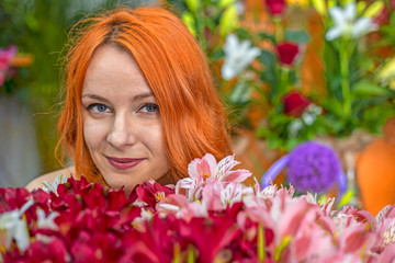 Obraz na płótnie Canvas Beautiful redhead Caucasian girl smelling colorful flowers in the garden 