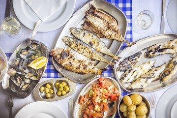 Barbecued sea bass, golden, horse mackerel accompanied with tomato salad, clams, bread and white wine
