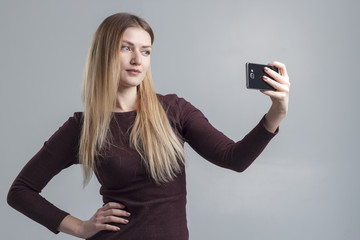 The girl makes selfie on the phone on a gray background, isolate