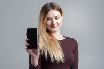 Fototapeta premium Close up portrait of a smiling woman showing screen mobile phone while standing isolated over gray background