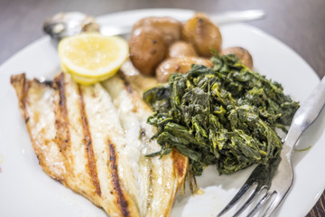 Barbecued sea bass served with lemon, baked potatoes and spinach