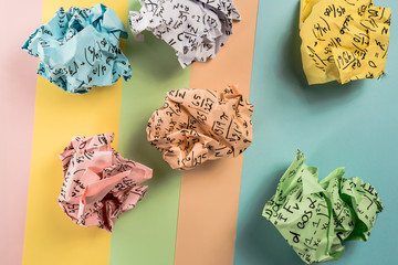 Crumpled multi colored paper balls with mathematical equations on multi colored plain paper, with...