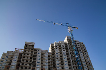 Fototapeta na wymiar cranes over a high block-of-flats on the blue sky background