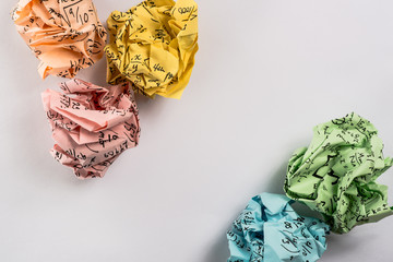 Crumpled multi colored paper balls with mathematical equations on multi colored plain paper, with...