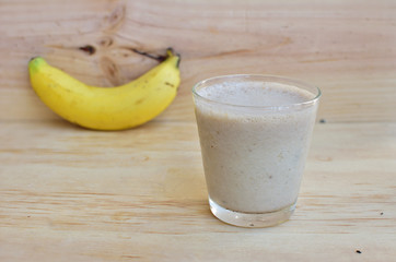 A Glass of fresh banana fruit smoothie on a rustic wooden background.