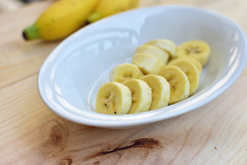 Sliced banana in white bowl on wooden background.
