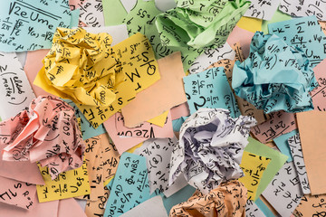 Crumpled multi colored paper balls with mathematical equations on multi colored plain paper, with soft texture. A bunch of multi colored torn paper with mathematical equations on it, background.