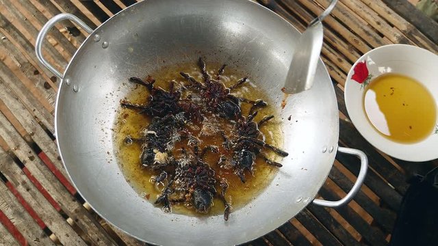 Woman turning over deep frying tarantulas inside a wok using a metal spatula (close-up upper view)
