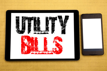 Hand writing text caption inspiration showing Utility Bills. Business concept for Money Bill Payment Written on tablet laptop, wooden background with sticky note, coffee and pen