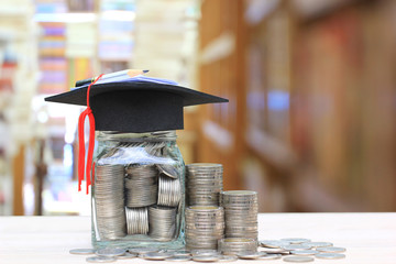 Graduation hat on the glass bottle on bookshelf in the library room background, Saving money for education concept