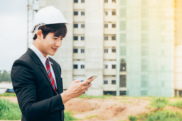 Fototapeta premium Asian engineer holding smartphone work concept teamwork of building construction. Project contractor reviewing plan work in construction site.