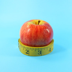 Red apple fruit and  tape measure  on blue background