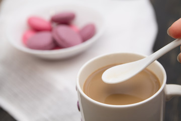 Good morning with a cup coffee with coffee-drops falling down from a spoon and pink macarons blurred on a black wooden background