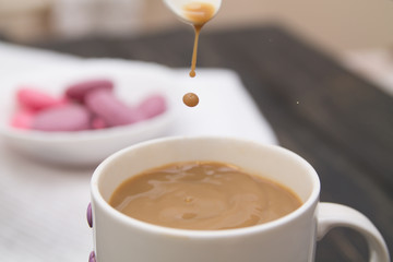 Good morning with a cup coffee with coffee-drops falling down from a spoon and pink macarons blurred on a black wooden background