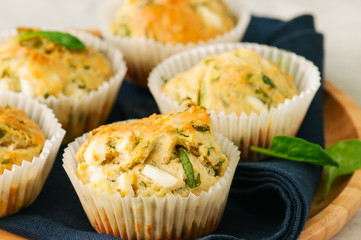 Savory muffins with feta cheese and spinach on a wooden plate on a wire rack.White stone backdrop.