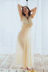 Fototapeta premium Young woman in retro pin up style and white dress poses against a white curtain backdrop