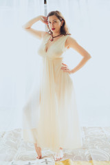 Fototapeta na wymiar Young woman in retro pin up style and white dress poses against a white curtain backdrop