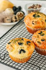 Savory muffins with olives and herbs on a wire rack on a white stone backdrop.