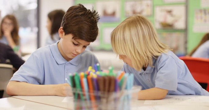 4K 2 little boys drawing together in elementary school classroom. Slow motion