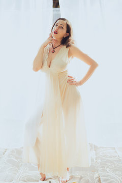 Young woman in retro pin up style and white dress poses against a white curtain backdrop