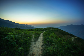 Road on spine and the top of the mountains covered with greenery with gentle valleys at dawn