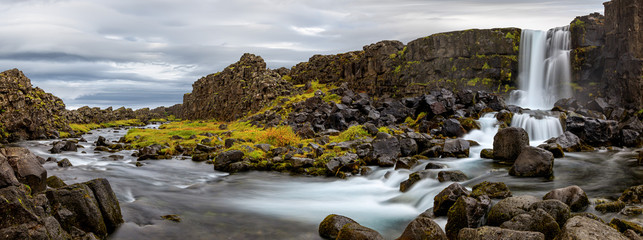 A panorama of Oxararfoss, Iceland with the fall plant colors popping against the black rocks, the...