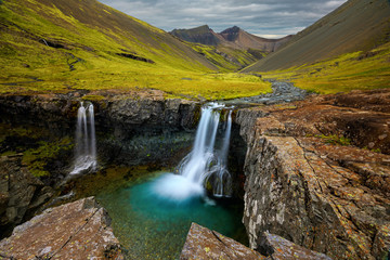 Fototapeta na wymiar Iceland waterfall through a gaping hole in the rock, into an aqua pool of glacier water