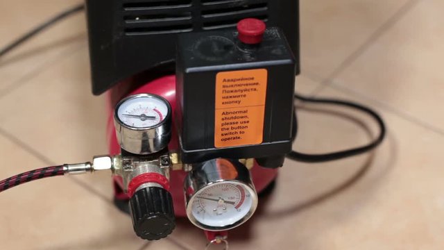 Man's hand turns on small portable piston-type air compressor standing on the floor